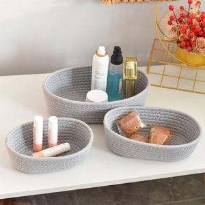 Three-piece set of grey woven cotton rope storage baskets in different sizes on a white desk