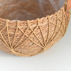 Detail of woven straw plant pot showing plastic liner and brown leather handles with rivets