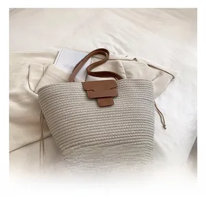 Close-up of a hand-woven straw tote bag featuring brown leather handles and side drawstrings