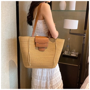 Detail of woven straw tote bag featuring brown leather shoulder straps and decorative tassels