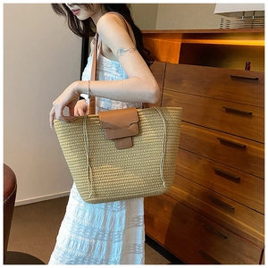 Detail shot of a large straw tote bag featuring brown leather straps and drawstring closure