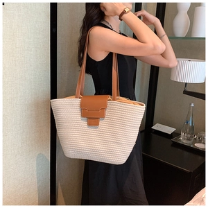 Close-up of woven straw tote bag featuring brown leather straps and magnetic closure
