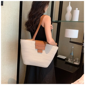 Close-up of a large woven tote bag with brown leather straps and a minimalist buckle flap