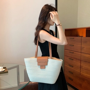 Large beige woven tote bag with brown leather handles worn by a model in casual style