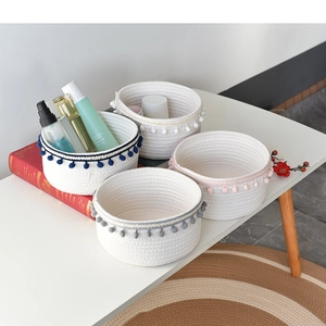 Detail of four colorful woven cotton rope baskets with decorative pompoms on white desk