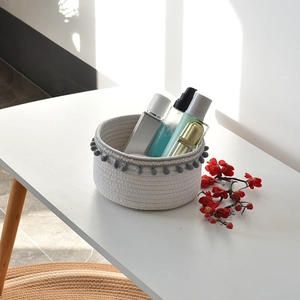 Detailed view of a white woven cotton rope storage basket with grey pom-pom tassels and skincare items