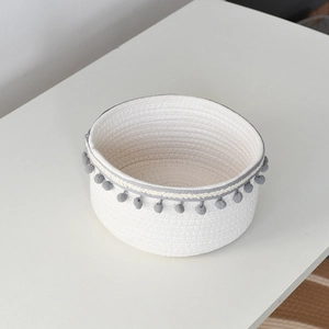 Top view of a white woven cotton storage basket with grey pom-poms and Nordic style fringe