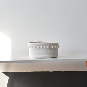 Close-up of white woven cotton rope storage basket featuring decorative pom-poms on the rim