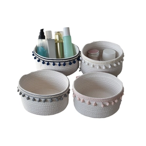 Set of four colorful cotton rope woven storage baskets with decorative pom-poms on the rim