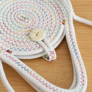 Gros plan détaillé des surpiqûres colorées et du bouton en bois gravé sur le sac en paille