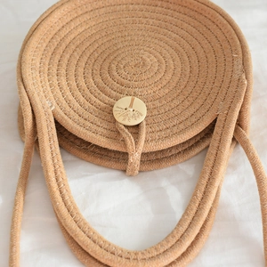 Détail d'un sac cabas rond en paille avec bouton en bois gravé et texture tressée