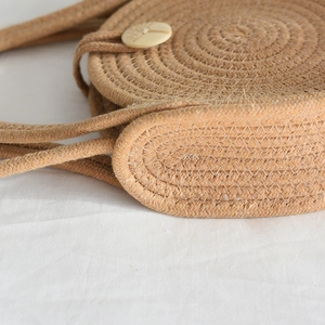 Détail d'un sac rond en paille tissé à la main montrant la texture et le bouton artisanal