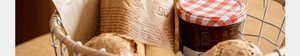 Detail of hand-woven bread basket with vintage newspaper wrap and fruit jam jar