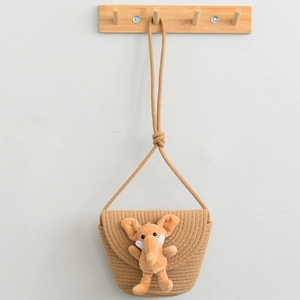 Detail of hand-woven straw crossbody bag for kids with cute orange elephant plush toy decor