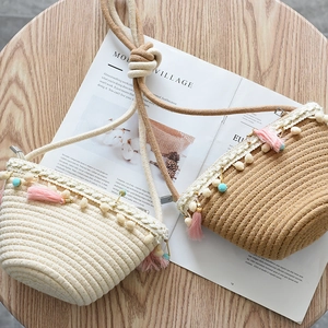 Detail of handmade straw crossbody bag with lace trim, pom-poms, and pink tassel