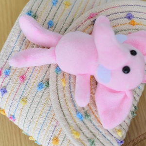 Close-up of pink plush elephant charm on beige straw bag with colorful pom-poms