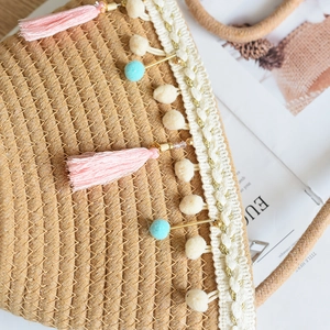 Close-up of kids straw bag with pink tassels, pom-poms, and lace trim for summer beach style
