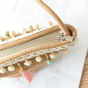 Detail of children's straw bag featuring metal zipper and cute cream pom-poms trim