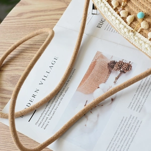 Detail of straw woven bag featuring lace trim, gold beads and colorful pom-poms