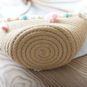 Close-up of handwoven straw bag featuring a spiral base and colorful tassel pom-poms