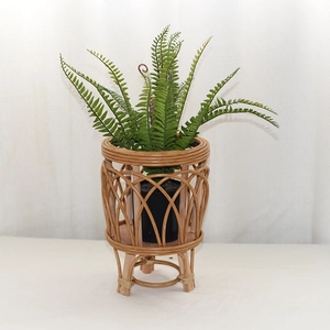 Detail of woven rattan plant stand with tripod wooden legs and artificial fern decoration