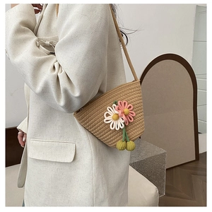 Detailed macro view of handmade straw crossbody bag with 3D knitted daisies and green pom-poms