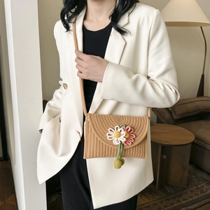 Detail of woven straw crossbody bag with 3D floral accents on a cream blazer