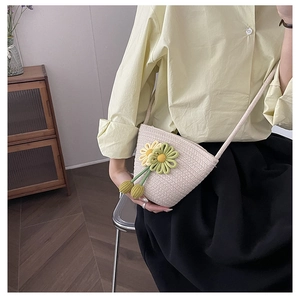 Detail of hand-woven beige crossbody bag featuring delicate daisy charm and rope strap