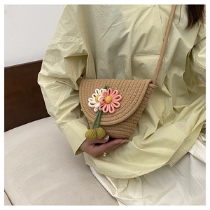 Detail of handmade woven straw crossbody bag with crochet pink flowers and green leaves