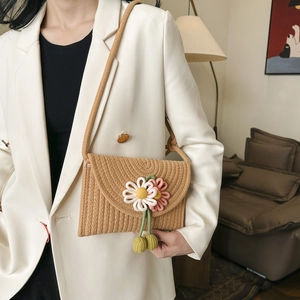 Detail of woven straw envelope bag with decorative floral accents and tassels on a model