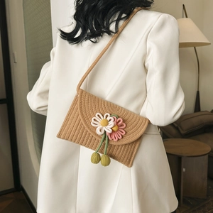 Detail of hand-woven straw crossbody bag with 3D floral accents and green pom-poms