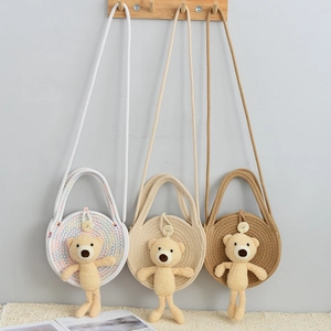 Close-up of woven straw round bags in three colors featuring cute plush bear charms