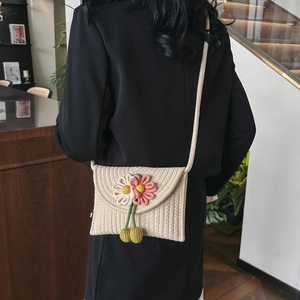 Close-up of woven crossbody phone bag with 3D daisy flower accents and green tassel
