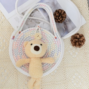 Close-up of white woven bag with colorful stitching, wooden button and plush bear charm