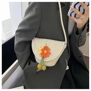 Detailed macro of handwoven straw crossbody bag featuring a vibrant orange flower pendant