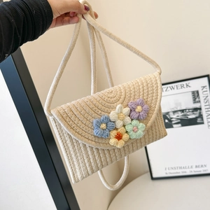 Detail of hand-woven straw crossbody bag with colorful crochet floral accents and long strap