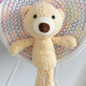 Detail of yellow fuzzy teddy bear charm on woven mat for a stylish straw crossbody bag