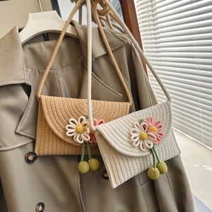 Detail of woven straw crossbody bags with daisy embroidery on khaki trench coat