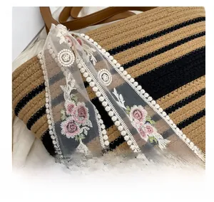 Détail du sac en paille tissé avec broderie florale en dentelle et bandoulière en cuir