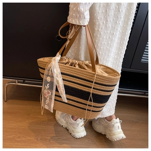 Détail du sac cabas en paille tissé avec rayures noires, anses en cuir et ruban dentelle