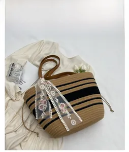 Détail du sac seau en paille tressée kaki avec écharpe en dentelle et anses en cuir brun