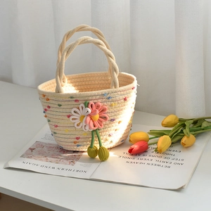 Détail du sac en coton tressé avec décor de marguerites et pompons verts sur table blanche