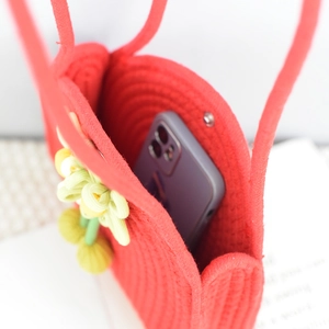 Close-up of red woven cotton rope handbag with magnetic buckle and floral charm