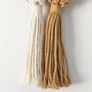 Detail of handmade cream and camel cotton tassels with woven texture on a wall hanging