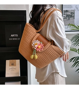 Detail of straw shoulder bag with leather flap and crochet flower decorations on model