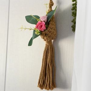 Detail of hand-woven brown macrame hanging basket with pink roses on white wall