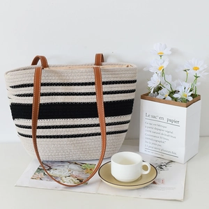 Detailed close-up of woven black and white striped tote bag with brown leather straps