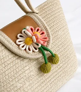 Detailed close-up of straw woven tote with leather flap and knit floral decorations