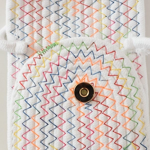 Detail der weißen geflochtenen Handytasche mit Regenbogennaht und goldenem Magnetverschluss