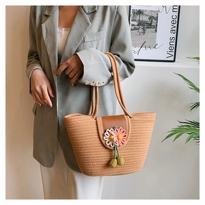 Detailed close-up of woven straw tote bag with leather buckle and floral knit charm